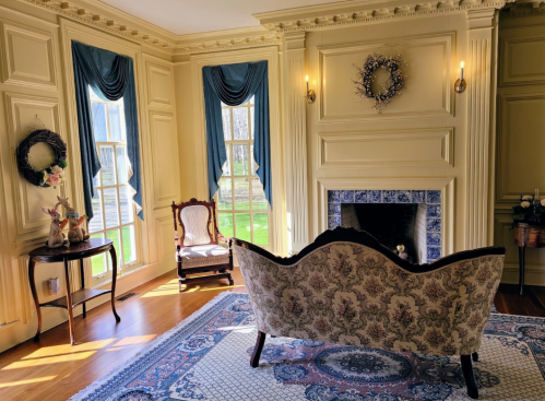 A cozy room with a patterned sofa, elegant curtains, and a fireplace, featuring a decorative wreath and a vintage chair.