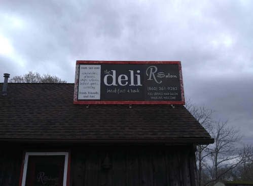 Sign for "the deli R Salon" offering breakfast and hair services, with a welcoming message and contact number.