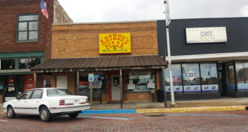 A brick building with a sign for "Arthur's Pizza Mexican Food" and a white car parked in front.