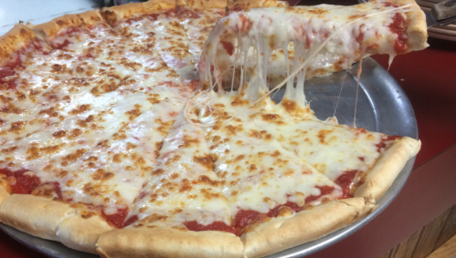 A large cheese pizza with gooey melted cheese and a slice being lifted, resting on a metal pizza tray.