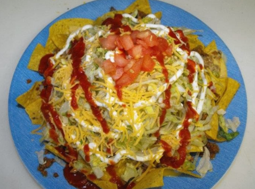 A colorful plate of nachos topped with lettuce, cheese, tomatoes, sour cream, and salsa.