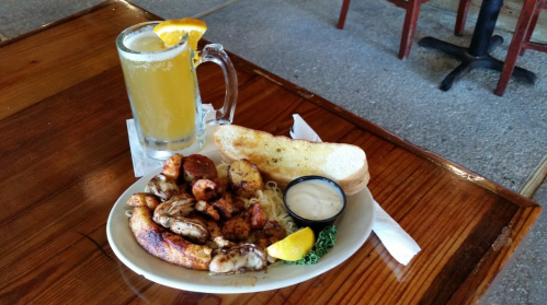 A plate of grilled shrimp and fish with a side of garlic bread, accompanied by a cold drink and lemon garnish.