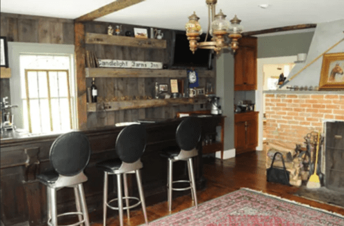 Cozy home bar with three stools, wooden walls, a brick fireplace, and rustic decor.