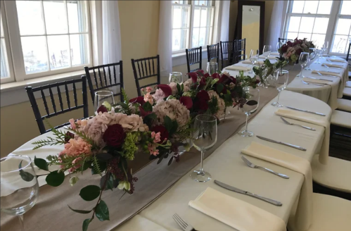 Elegant dining setup with a floral centerpiece, white tablecloths, and glassware in a bright, inviting room.