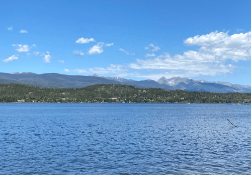 A serene lake surrounded by mountains under a clear blue sky with scattered clouds.