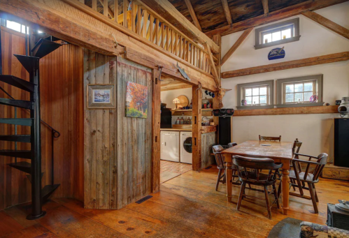Cozy interior of a rustic cabin featuring wooden beams, a spiral staircase, and a dining area with a wooden table and chairs.