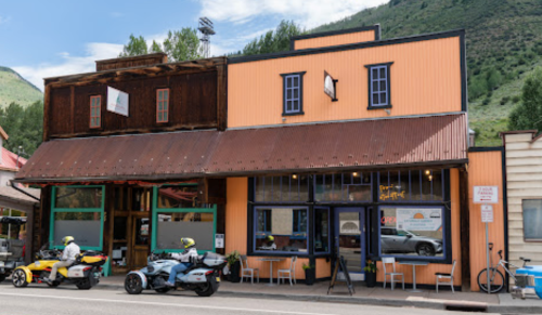 A colorful building with a metal roof, featuring outdoor seating and two motorcycles parked in front.