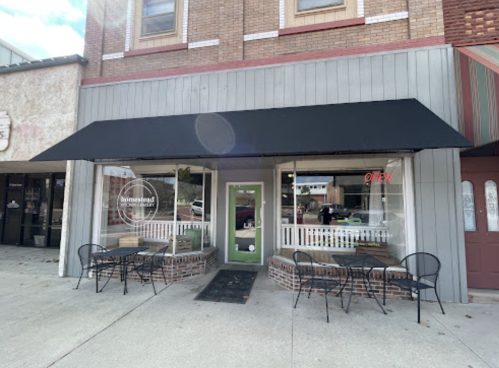 A storefront with a black awning, green door, and outdoor seating, featuring an "Open" sign in the window.