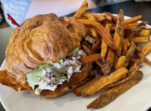 A croissant sandwich filled with chicken salad and lettuce, served with a side of crispy sweet potato fries.