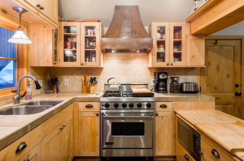 Cozy kitchen with wooden cabinets, stainless steel appliances, and a large range hood over a gas stove.