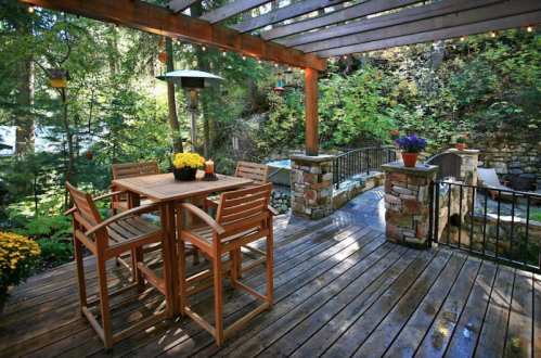 A wooden deck with a table and chairs, surrounded by greenery and stone features, creating a cozy outdoor space.