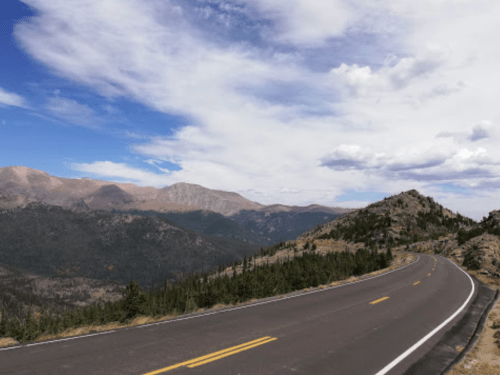 A winding road curves through a mountainous landscape under a partly cloudy sky.