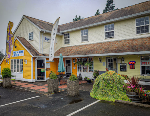 A charming yellow and white building with a pie shop sign, outdoor seating, and colorful flags in a quaint setting.