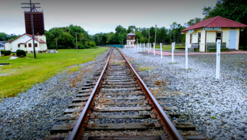 A view of a railway track leading to a small station surrounded by greenery and gravel.
