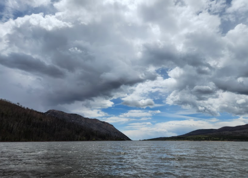 A serene lake surrounded by mountains under a cloudy sky, with patches of blue peeking through the clouds.
