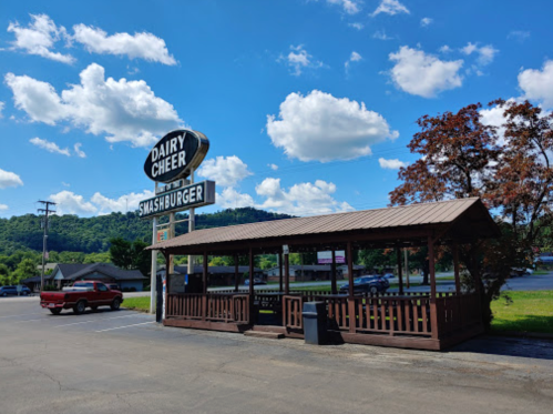 A wooden outdoor seating area at Dairy Cheer, featuring a sign for Smashburger, under a blue sky with fluffy clouds.