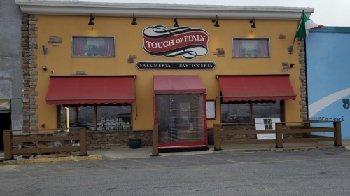 Exterior of "Touch of Italy" restaurant featuring a yellow facade, red awnings, and a stone accent wall.