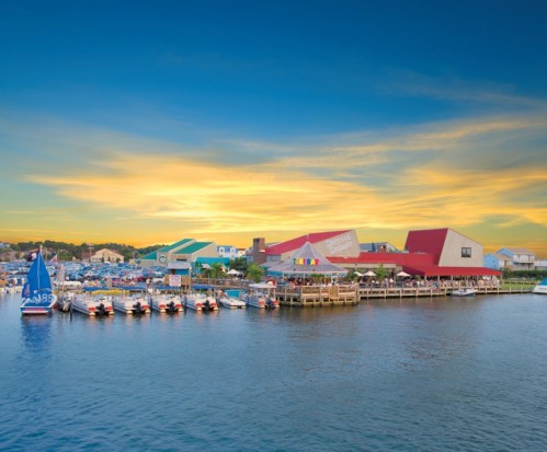 A scenic waterfront view featuring boats docked by colorful buildings under a vibrant sunset sky.