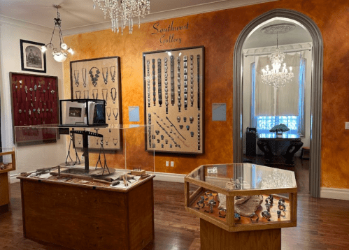 Interior of a gallery featuring displays of jewelry and artifacts, with orange walls and elegant lighting.