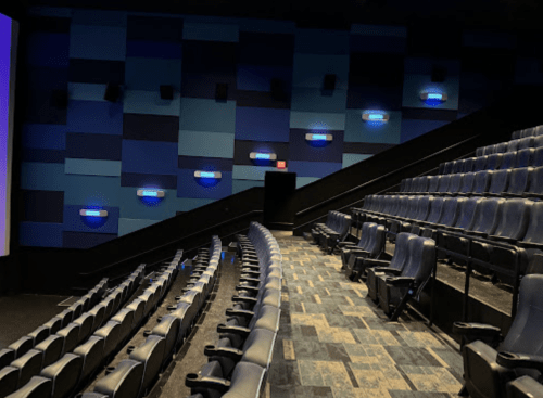 Interior of a movie theater showing empty rows of blue seats and a colorful wall with dim lighting.