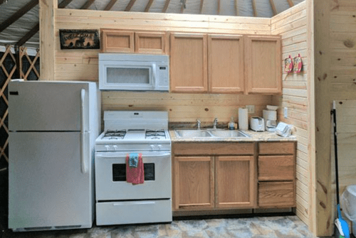A cozy kitchen with wooden cabinets, a stove, microwave, sink, and refrigerator in a rustic setting.