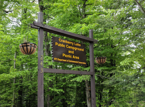 Sign for Cranberry Lake Public Campground and Picnic Area, surrounded by lush green trees.