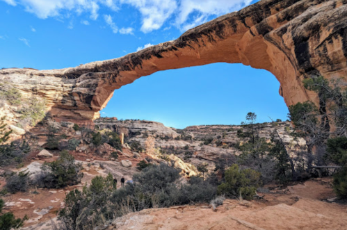 Natural stone arch towering over a rocky landscape with sparse vegetation and a clear blue sky.