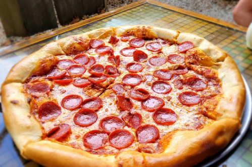 A large pepperoni pizza with a golden crust, sliced into eight pieces, on a checkered table.