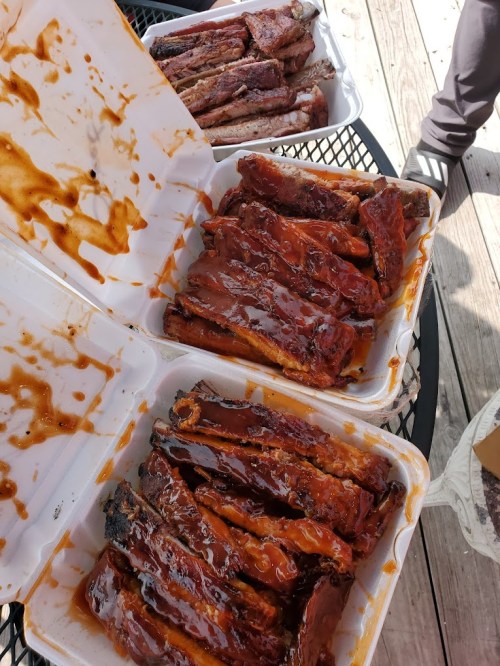Three containers of glazed barbecue ribs, stacked on a table, with sauce drizzled over the meat.