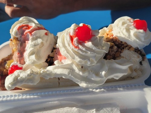 A delicious banana split topped with whipped cream, cherries, and crunchy toppings, served in a white dish.