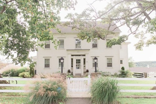 A charming two-story white house with a front yard, surrounded by greenery and a white picket fence.