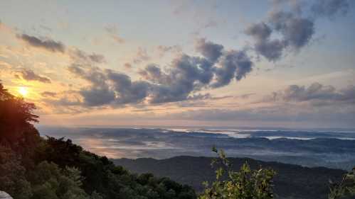 A scenic view of rolling hills and valleys at sunrise, with clouds and mist creating a serene atmosphere.