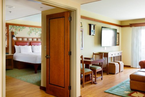 A cozy hotel room featuring a bedroom with a bed, a living area with a dining table, and wooden decor.