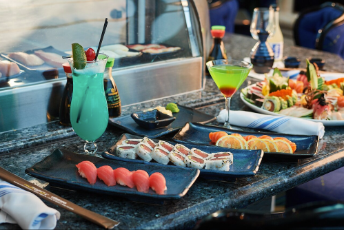A vibrant sushi spread featuring various rolls, sashimi, and colorful cocktails on a marble table.