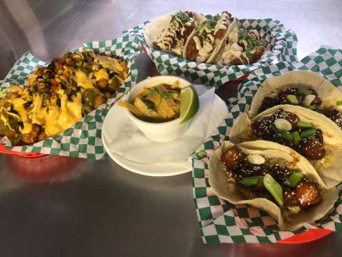 A variety of tacos and nachos served on checkered paper, with a side of tortilla chips and lime.