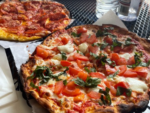 Two pizzas on a black table: one with pepperoni and the other topped with tomatoes and basil.