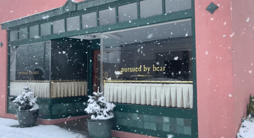 A cozy restaurant with a green facade and gold lettering, surrounded by snow and winter decor.