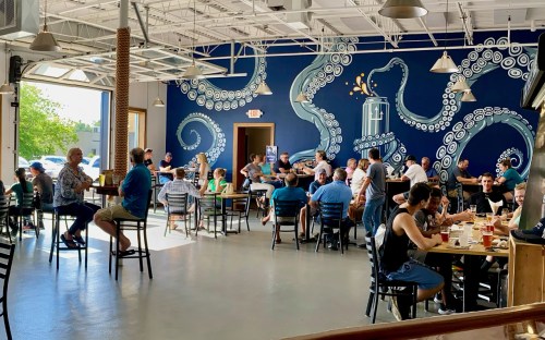 A lively brewery interior with patrons enjoying drinks, featuring a large octopus mural on the wall.