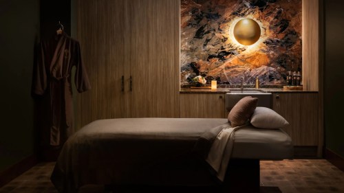 A serene spa room featuring a massage table, warm lighting, and a decorative stone wall.