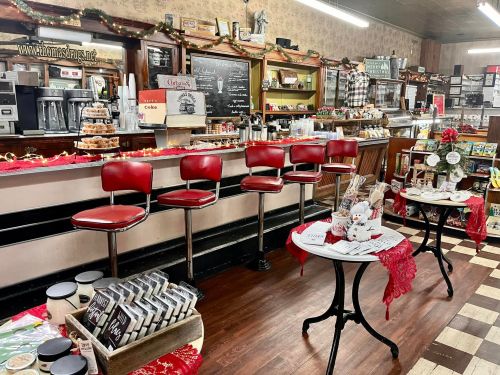 Cozy café interior with red bar stools, a counter filled with baked goods, and festive decorations.