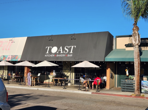Exterior of Toast Kitchen Bakery Bar with outdoor seating and umbrellas on a sunny day.
