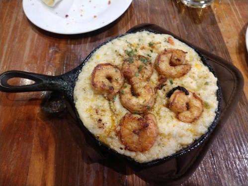 A cast iron skillet filled with creamy grits topped with grilled shrimp and garnished with herbs.