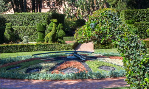 A landscaped garden featuring topiary sculptures and a decorative sundial surrounded by vibrant greenery.