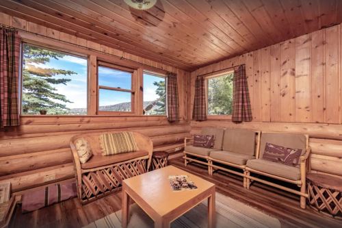Cozy wooden cabin interior with a seating area, large windows, and scenic views of nature outside.