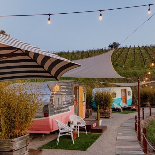 Vintage trailers in a vineyard setting, surrounded by string lights and greenery, creating a cozy outdoor atmosphere.