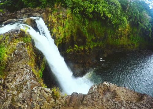 A scenic waterfall cascading into a serene pool, surrounded by lush greenery and rocky terrain.