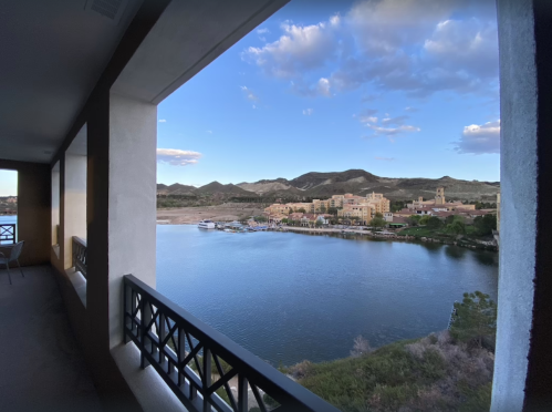 View from a balcony overlooking a serene lake, mountains, and a charming village under a clear blue sky.