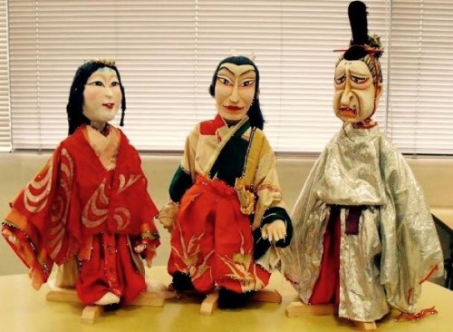 Three traditional puppets dressed in colorful costumes, showcasing intricate designs and expressive faces, displayed on a table.