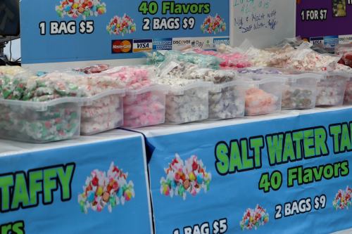 A display of colorful saltwater taffy in clear containers, with pricing signs for different bag options.