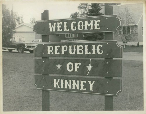 Black and white photo of a sign reading "Welcome Republic of Kinney" with decorative lettering.